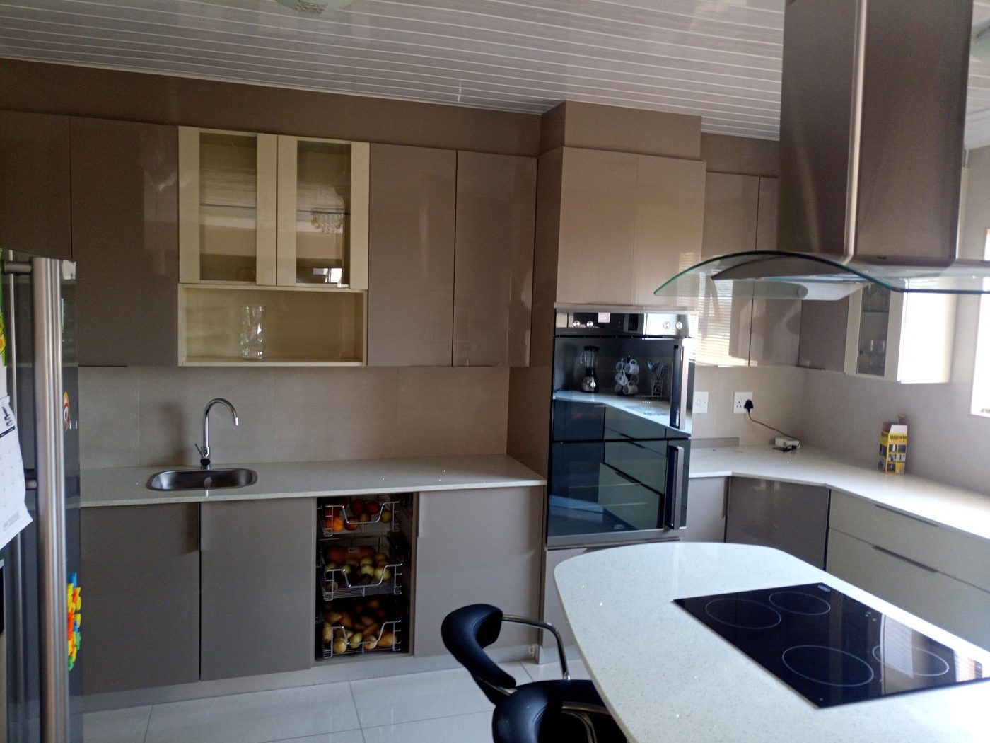 Mocha gloss kitchen with glass-front wall units, wire vegetable baskets and a curved island
