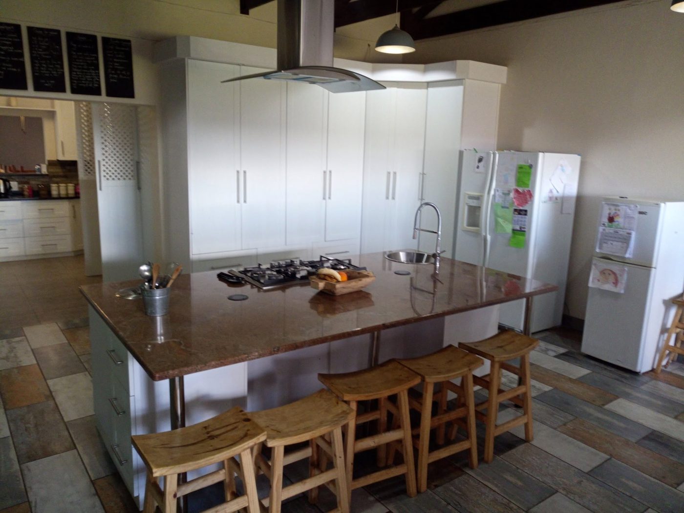 Country style kitchen with tall white cupboards and a large granite-topped island with bar stools
