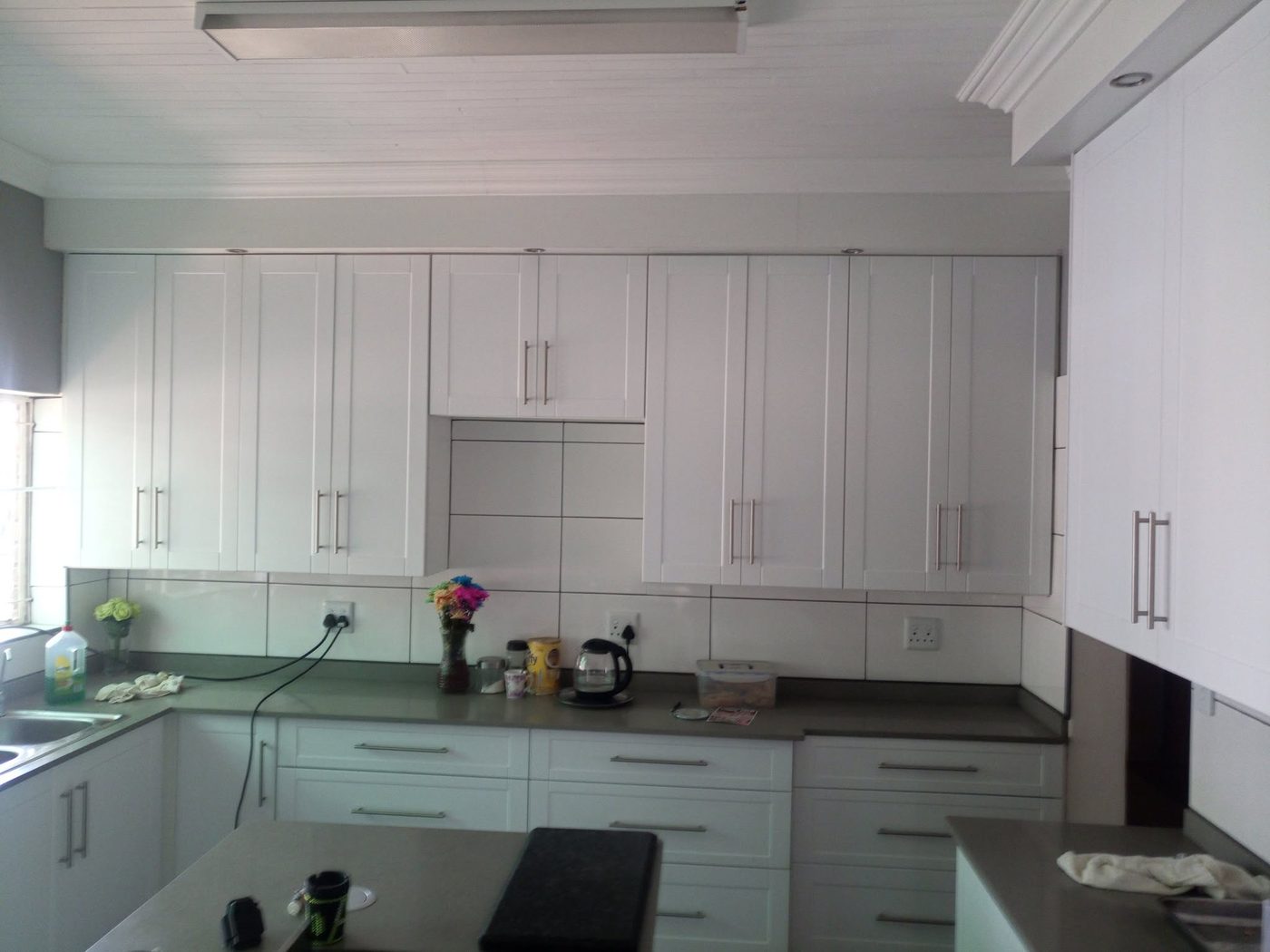 White shaker-style kitchen cupboards with brushed steel handles and a grey worktop