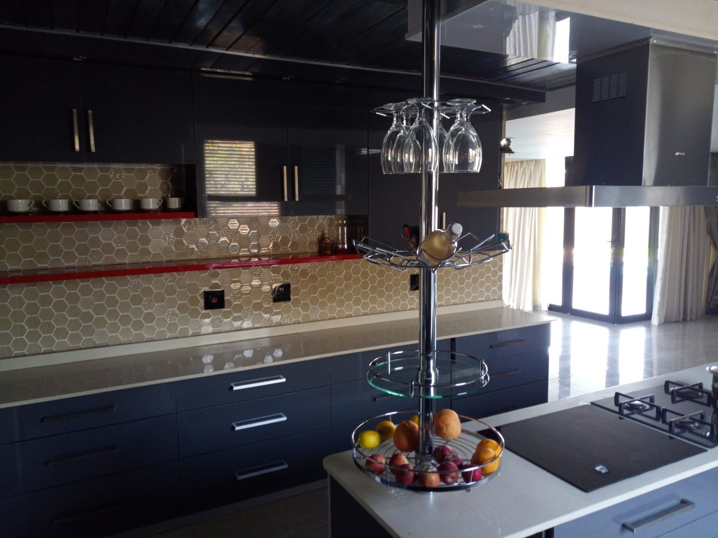 Dark grey gloss kitchen with hexagon mosaic splashback and red accent shelves